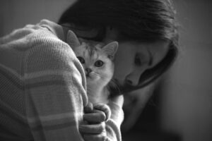 Foto preto e branca de uma mulher triste abraçando um gato.