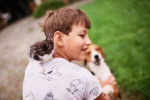 Menino com gato no ombro e um cachorro, ao fundo, olhando para eles.