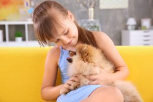 Menina sentada no sofá com Lulu da Pomerânia no colo.
