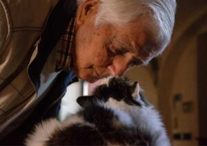 Idoso triste cheirando um gato.