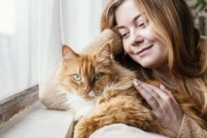 Mulher com gato Maine Coon, ambos na janela.