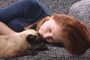Mulher deitada no sofá com gato siamês.